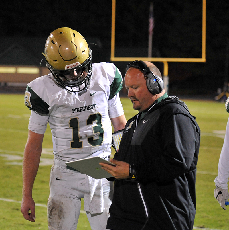 A coach and a player reviewing plays together on a tablet on the sideline