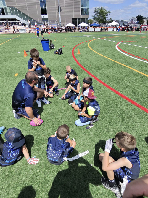 A youth football coach talking with his team on the sideline
