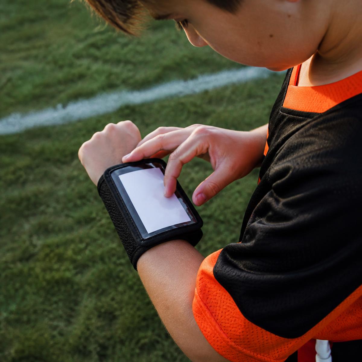 Youth football player checking a play wristband on his forearm